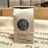 Product Shot: Recycled kraft bag filled with fresh roasted coffee, labelled "Bolivia Caranavi Dark", branded with a She Grows Coffee stamp, and stamped with a roast date.