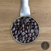Close-up shot of Bolivia Caranavi dark roasted coffee beans in a handmade scoop with a wooden cutting board background.