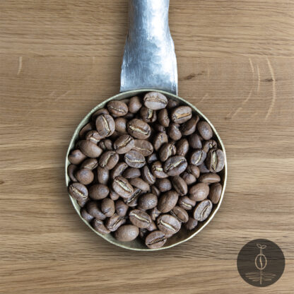 Close-up shot of Colombia Sierra Nevada light roasted coffee beans in a handmade scoop with a wooden cutting board background.