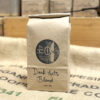 Product Shot: Recycled kraft bag filled with fresh roasted coffee, labelled "Dark Arts Blend", branded with a She Grows Coffee stamp, and stamped with a roast date.