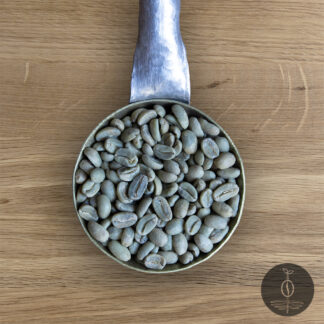 Close-up shot of Papua New Guinea Kainantu green (raw) coffee beans in a handmade scoop with a wooden cutting board background.