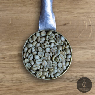 Close-up shot of Honduras Marcala Finca Adolfo green (raw) coffee beans in a handmade scoop with a wooden cutting board background.