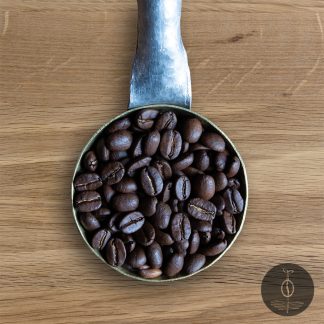 Close-up shot of Papua New Guinea Korgua Estate AA medium roasted coffee beans in a handmade scoop with a wooden cutting board background.