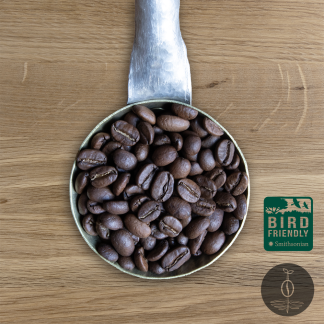 Close-up shot of Honduras Marcala Bird Friendly certified light-medium roasted coffee beans in a handmade scoop with a wooden cutting board background.