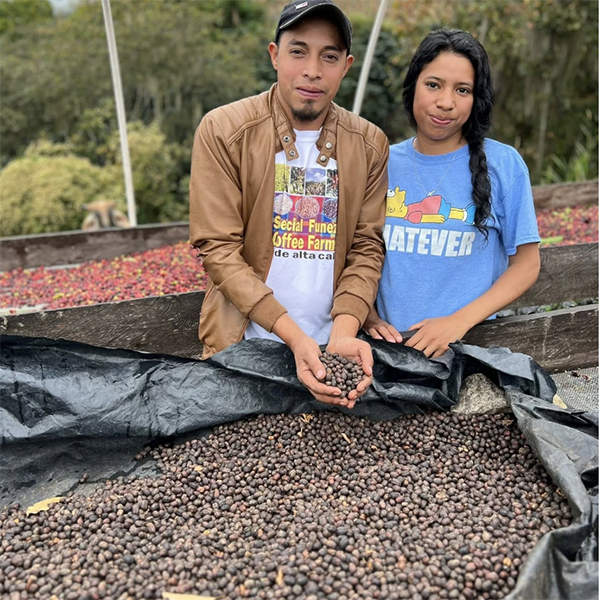 Coffee grower, Josue Ariel Funez, posing with his family member and showing a natural process coffee drying on a raised bed.