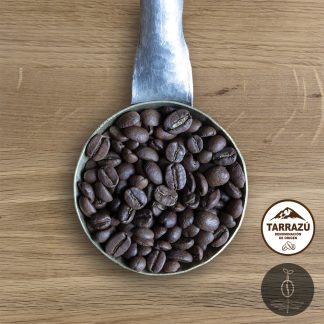 Close-up shot of Costa Rica La Pastora medium roasted coffee beans in a handmade scoop with a wooden cutting board background.